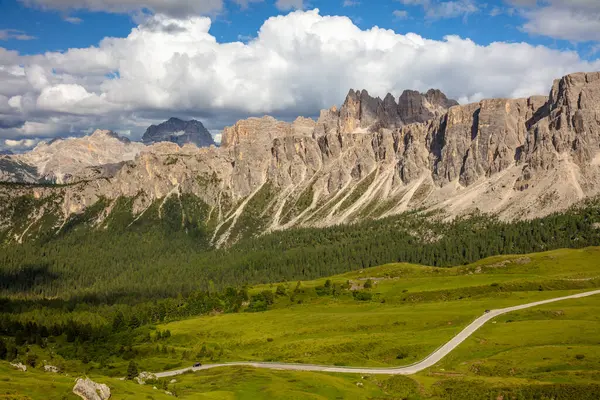 Avusturya Alplerinde güneşli bir yaz günü. Kayalık tepelerde desenli bulutlar. Yeşil bir vadide dolambaçlı bir yol