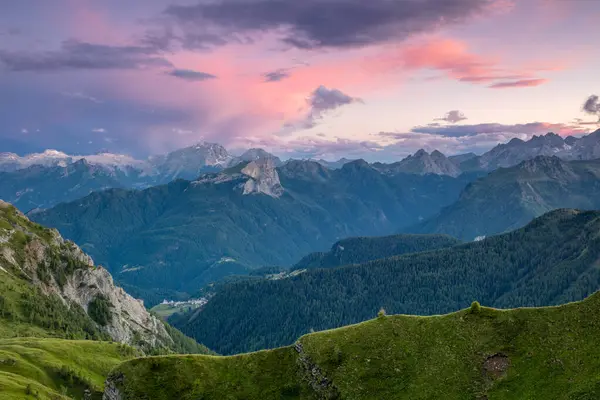 Avusturya Alplerinde yaz akşamı. Kayalık tepelerin üzerinde günbatımı fırtınalı gökyüzü. Orman ve çimlerle kaplı yeşil yamaçlar.