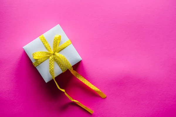 Gift box with yellow ribbon on pink background with space for message. Holiday greeting card for Valentine\'s, Women\'s, Mother\'s Day, Easter. Happy birthday. Valentine\'s Day. Top view, flat lay.