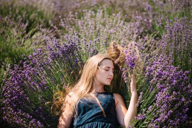 Mor lavanta tarlasında uzanan güzel elbiseli kız. Fransa 'da gün batımında lavanta tarlasında güzel bir kadın. Yumuşak odaklanma. Çiçeklerin tadını çıkar, yaz doğası. Kapat..