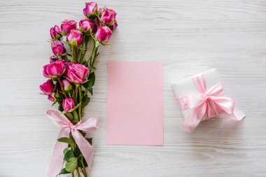 Pembe küçük güller, hediye kutusu, beyaz ahşap arka planda kartpostal. Doğum günün kutlu olsun. Bayram tebrik kartı, sevgililer günü, kadınlar, anneler günü, paskalya. Mesaj için yer açın. Üst manzara, düz uzanma.