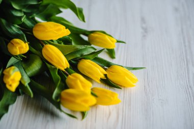 Bouquet of yellow tulips on white rustic wooden background with space for message. Summer flowers concept. Hello Spring. Holiday greeting card for Valentine's, Women's, Mother's Day, Easter. Side view