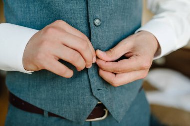 Adamların elleri düğmeleri bağlıyor. Takım elbiseli damat, gömlek. Klasik erkek giyim tarzı. Yarı işadamı sabah bir iş gününe ya da düğüne hazırlanır..