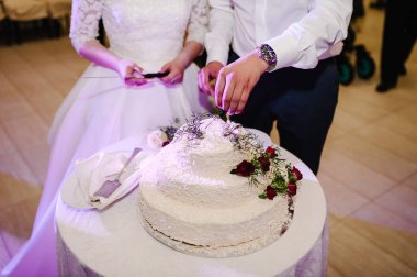 Gelin ve damat düğün ziyafetinde köy pastalarını kesiyorlar. Eller beyaz pastayı kırmızı çiçeklerle keser..