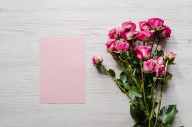 Craft pink postcard with bouquet of small roses on wooden background. Space for text message. Spring flowers. Holiday greeting card for Valentines, Women's, Mother's Day, Easter! Top view, flat lay.