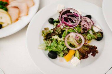Beyaz tabakta gurme salatası. Peynir dilimleri, marul. Beyaz masada beyaz tabak. Yiyecekler. Tatil günü. Düz yat. en üstteki görünüm.