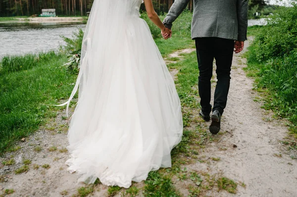 下のカップルの新婚夫婦の花嫁と新郎が緑の公園の歩道を歩いて戻って表示されます 幸せと喜びの結婚式の瞬間 — ストック写真