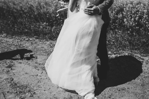 新郎新婦の脚は 結婚式の後に戻って歩く下のドレス 最高の結婚式の日 新婚夫婦は新婚旅行のために田舎の直線道路にいる リアビューだ 黒い白い写真 — ストック写真