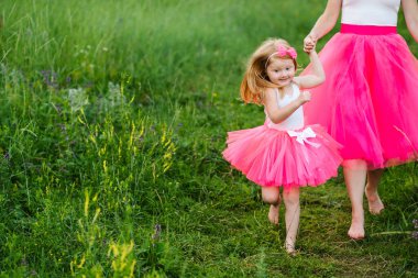 Pembe elbiseli ve tarlada yalınayak yürüyen bir anne. Aynı kıyafetleri giyen bir kızı olan genç ve güzel bir anne. Aile görünüşü aynı. Moda tarzı. Ebeveynler ve çocuklar için giysi.