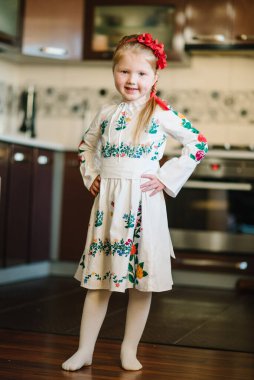 Ukrayna folkloru işlemeli bir elbise giymiş fotoğraf için poz veren sevimli bir kızın portresi. Evde başında haşhaş çelengi olan bir çocuk. Ulusal etnik geleneksel kostüm veya elbise.