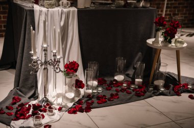 Mum ışığında romantik bir akşam yemeği. Masa gül yapraklarıyla bir masa örtüsüyle süslenmiş. Etkinlik için lüks bir dekor. Evlilik teklifi için bir sürpriz. Sevgililer gününde çift için masayı hazırla..