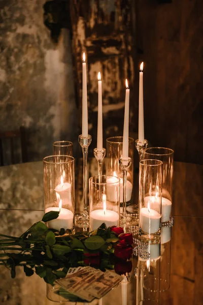 Luxurious rustic style table on background of evening lighting in restaurant for gala dinner. Mirror table for a party. Chic table is decorated with candles, flowers and money for wedding invitations.