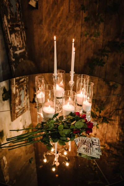 Mirror table for party. Luxury rustic style table on background of evening lighting bulbs in restaurant for gala dinner. Chic table is decorated with candles, flowers and money for wedding invitations
