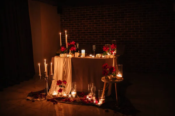 Location for a surprise proposal at night. Decoration flowers, burning candles. Luxury romantic date. Table setting in restaurant for event. Candlelight for couple on Valentines day.