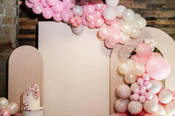 Arch decorated with pink, brown balloons. Cake is decorated bear figure, rainbow. Trendy baptism cake for girl. Delicious reception at a birthday party. Photo wall decoration space or place for text.