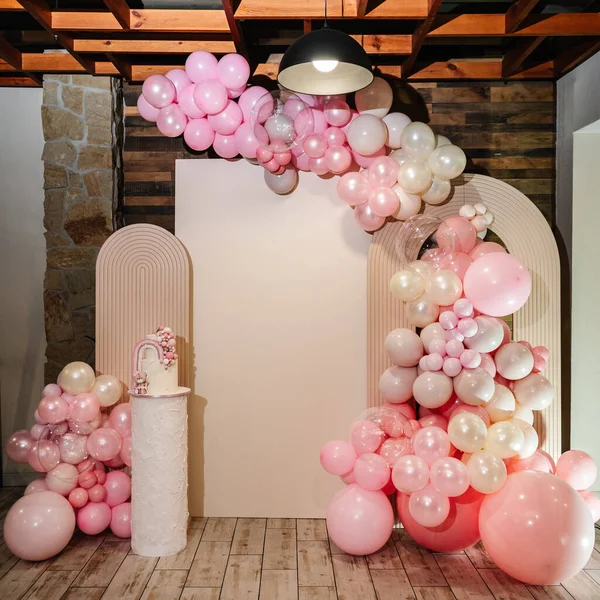 Arch decorated with pink, and brown balloons, decor rainbow. Trendy baptism cake for girl. Photo wall decoration space or place for text. Celebration concept. Delicious reception at a birthday party.