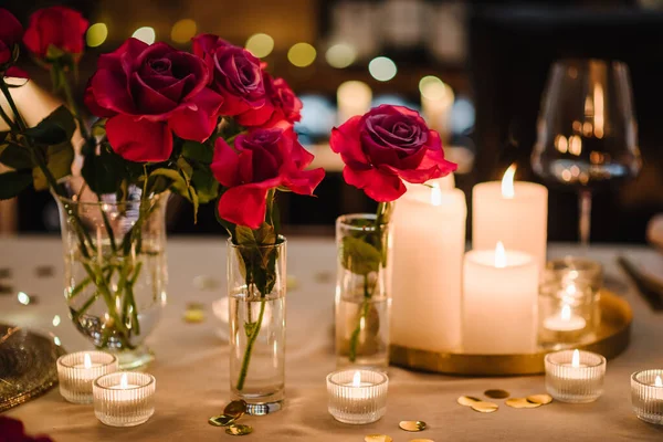 Burning candles for surprise marriage proposal. Luxury candlelight date in restaurant. Bokeh, garlands, bouquet flowers. Romantic dinner setup at night. Table set for couple, Valentine\'s Day evening.