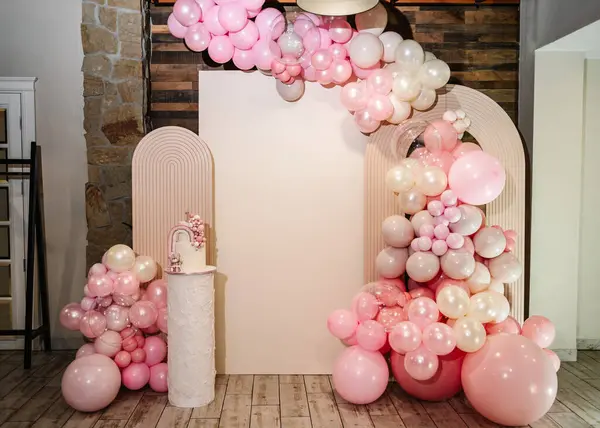 Arch decorated with pink, brown balloons. Photo wall decoration space or place for text. Cake is decorated bear figure, rainbow. Trendy cake for 1 old years girl. Delicious reception at birthday party