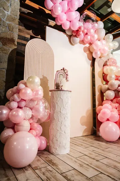 Arch decorated with pink, brown balloons. Photo wall decoration space or place for text. Cake is decorated bear figure, rainbow. Trendy baptism cake for girl. Delicious reception at a birthday party.