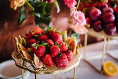 Meyveli bir tabak, çilek, erik, incir. Çikolata yakın plan. Lezzetli bir düğün töreni. Arka plan dekoru. Şölende doğum günü partisi için süslenmiş pembe çiçekler..