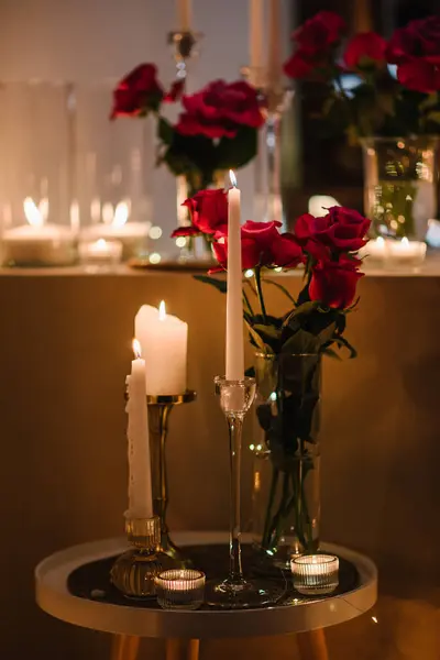 Decoration flowers, burning candles, details closeup. Luxury romantic date. Location for a surprise proposal at night. Table setting in restaurant for event. Candlelight for couple on Valentines day.