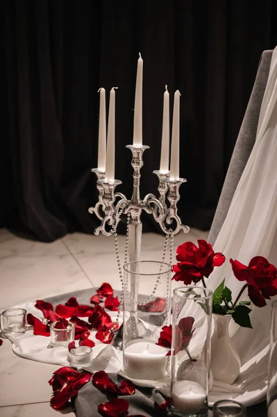 Detail decor. Romantic dinner by candlelight. Table decorated with tablecloth with rose petals. Luxurious decor for event. Surprise for marriage proposal. Set up for couple on evening Valentine's day