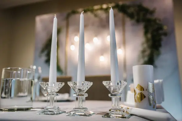 Three candles on table. Festive table decorated composition flowers and candles in party area. Wedding setup detail. Table setting, serving closeup. Banquet decoration in hall. Luxury reception.
