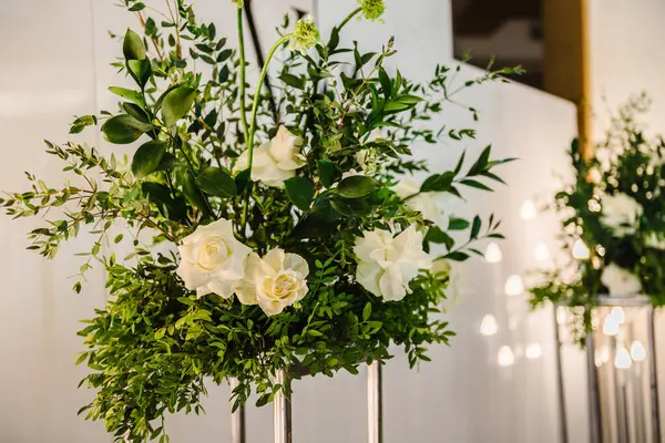 Decor of flowers and greenery for a wedding ceremony in a restaurant. The metal arch is decorated white and green flowers and garlands with light bulbs. Details interior closeup.