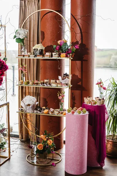 Delicious wedding reception luxury ceremony. Background decor. Candy bar. Table with sweets, candies, dessert. Arch decorated pink, orange flowers roses for birthday party in banquet area, hall.