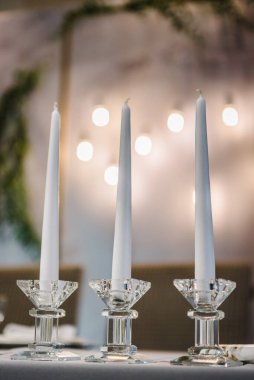 Masada üç mum var. Parti alanında şölen masası süslenmiş kompozisyon çiçekleri ve mumlar. Düğün hazırlıkları. Masa ayarı, yakın çekim. Salonda ziyafet dekorasyonu. Lüks resepsiyon.
