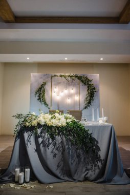 Yeni evliler düğün davetlerinde ziyafet alanında masa örtüsüyle kaplanırlar. Kemer süslü kompozisyon çiçekleri ve yeşillikle süslü masa, salon restoranında mumlar. Masa ayarı, resepsiyon.