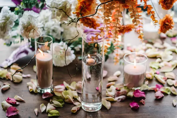 Candles, rose petals on floor. Closeup decor detail. Photo wall, arch decorated pink, orange flower for birthday party in banquet area, hall. Wedding reception for luxury ceremony. Decoration of event