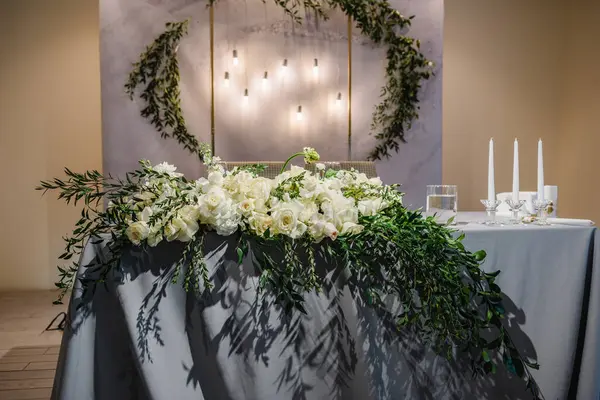 Festive table with arch decorated composition flowers and greenery, candles in hall restaurant. Table newlyweds covered with a tablecloth in banquet area on wedding party. Table setting, reception.