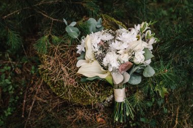Çiçekli düğün buketi güller ve yeşil çimenli yeşil kurdeleler. Üst Manzara. Düğün yüzükleri gelin ve damat arka plandaki gelin buketinde. Yosun ve Noel ağaçlarının iğnelerinde yüzükler