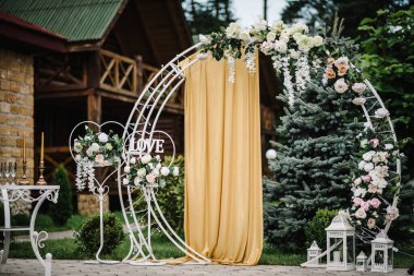 Kemer süslenmiş beyaz çiçekler, yeşiller, yeşillik, mumlar. Lüks düğün töreninin yapılacağı yer. Arka bahçede moda bir dekor. Boşluğu olan bir fotoğraf duvarı. Kutlama konsepti. Doğum günü partisi resepsiyonu.