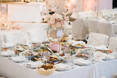 Düğün hazırlığı. Masa servisi. Salon restoranında ziyafet dekorasyonu. Lüks resepsiyon. Parti alanında şölen masası dekore edilmiş kompozisyon çiçekleri. Altın geometrik dekoratif işaret tablosu.