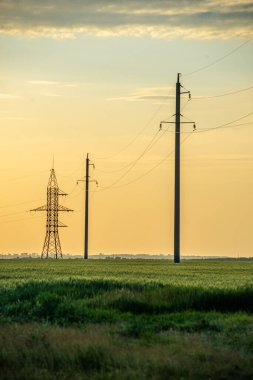 Gün batımında tarlada yüksek voltaj kulesi
