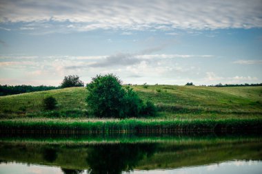 Yeşilliklerle çevrili güzel bir göl ve gün batımında bulutlu bir gökyüzü.