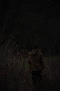 Siyah ceketli bir adam sonbahar ormanında yürüyor.