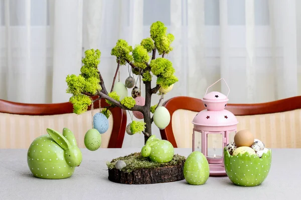 stock image Easter decoration in tree shape with hanging eggs. Ceramic figurines and painted eggs on the table. Postcard motif.