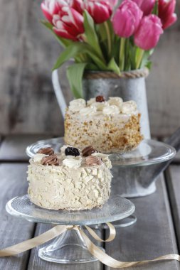 Pasta standında yuvarlak cappuccino keki. Arka planda güzel bir buket pembe ve kırmızı laleler. Parti zamanı