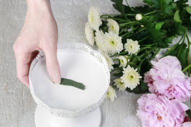 Kadın, bir buketi sabitlemek için iğne tutucuyu nasıl kullanacağını gösteriyor..