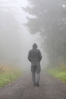 Adam sisin içinde duruyor, parktaki sokağa bakıyor. Sonbahar zamanı