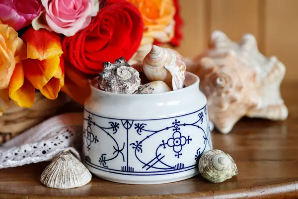 A bowl with sea shells, flowers in the background. A sentimental souvenir from a holiday by the sea.