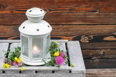 Kırsal ahşap masadaki yabani çiçeklerin arasında mumlu güzel bir fener. Parti dekoru
