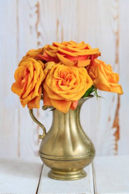 Altın vazoda bir buket turuncu gül. Ahşap arka plan. Ev dekoru
