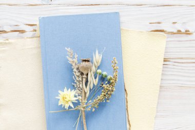 Kurumuş bitkiler ve çiçekler kumaş kapaklı mavi bir kitabın üzerinde. Grafiksel kaynaklar