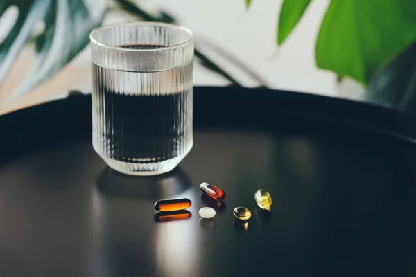 Health support and treatment during long winter. Morning dose of vitamin. Dietary supplements omega 3,6,9 and vitamin E and D3 mk2 and coco oil in capsules with glass of water on the table at home interior.