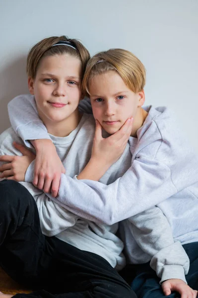 Two happy boys, happy brothers who are seriosly happily together. Brothers sit on grey background. modern tenagers. book cover. hug each other