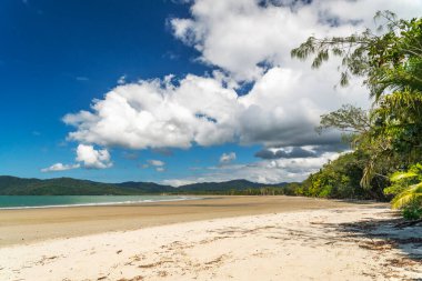 Daintree yağmur ormanlarında beyaz bulutlu mavi gökyüzü altında Queensland, Avustralya 'da tropikal altın kumlu bir sahil. Thornton Sahili güneyde Cape Tribulation Yolu ve doğuda Mercan Denizi ile çevrilidir..